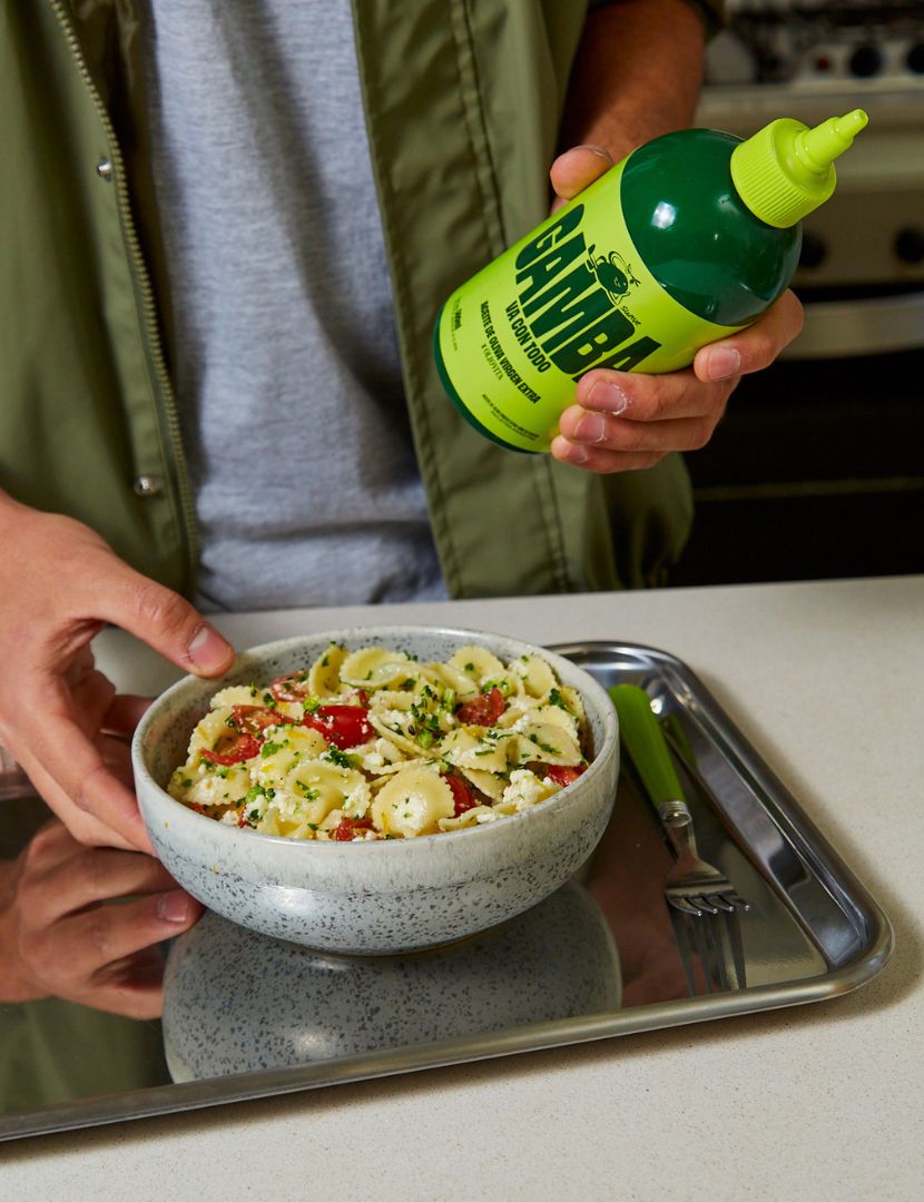 Una persona sostiene un bowl de ensalada de pasta y la botella squeeze de Gamba