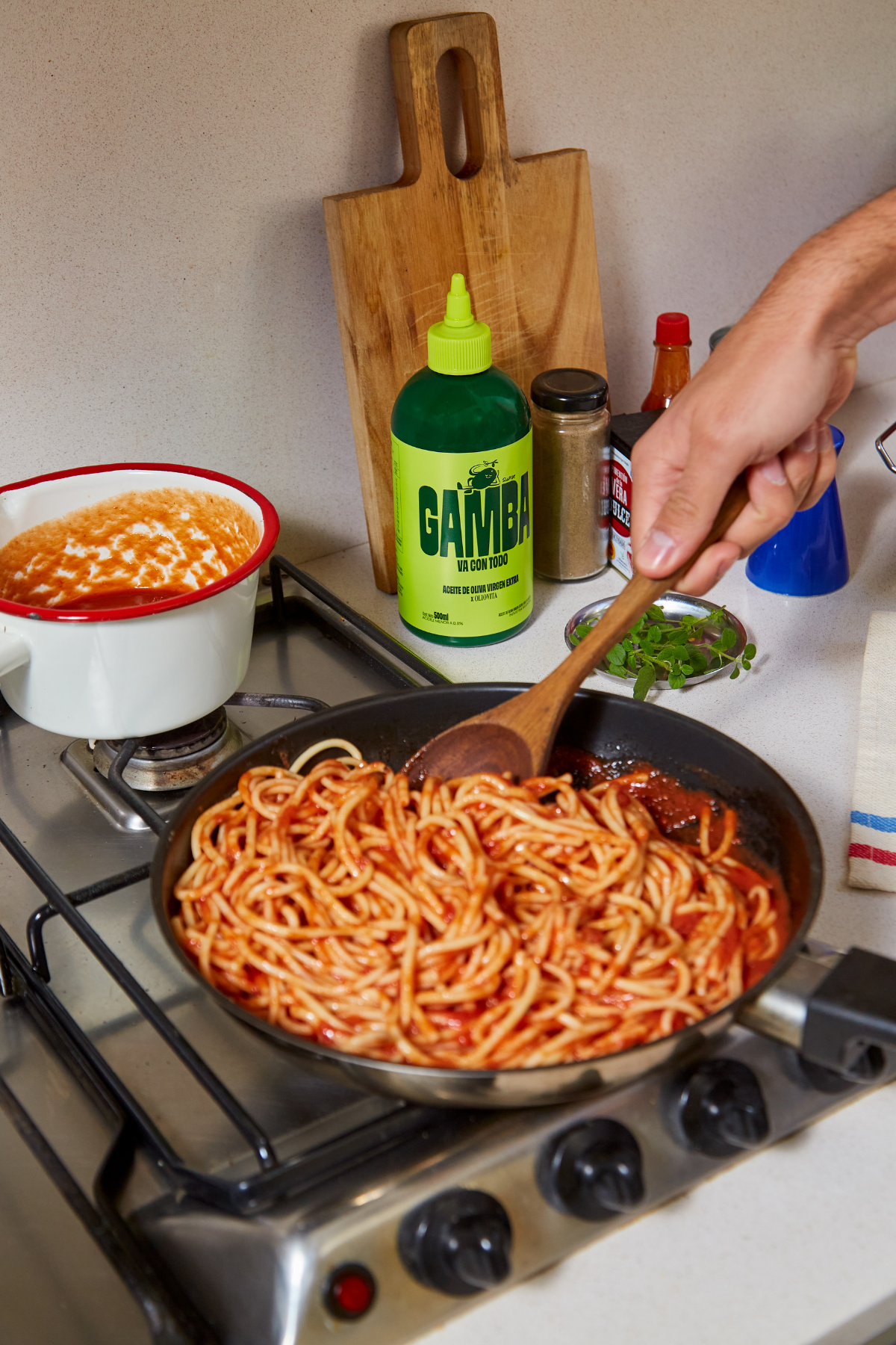 Sarten con fideos al tomate en la hornalla y la botella squeeze de Gamba sobre la mesada