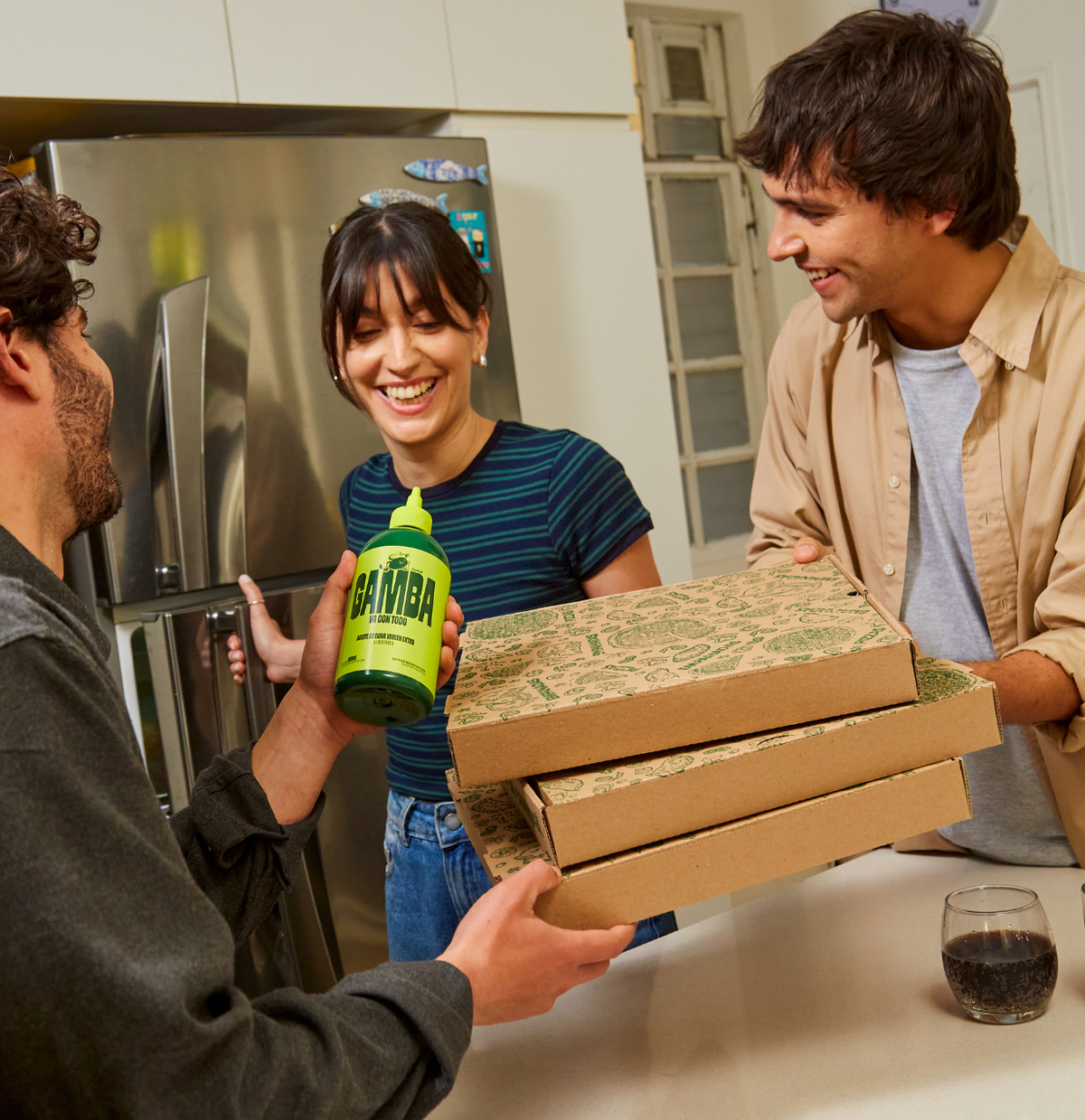 Tres personas reciben cajas de pizza en la cocina, con la botella squeeze de Gamba en la mano
